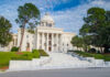 Exterior view of a historic government building with a dome and landscaped grounds