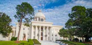 Exterior view of a historic government building with a dome and landscaped grounds