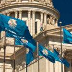 Oklahoma state flags waving in front of the State Capitol building