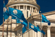 Oklahoma state flags waving in front of the State Capitol building