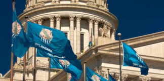 Oklahoma state flags waving in front of the State Capitol building