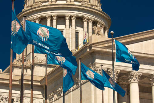 Oklahoma state flags waving in front of the State Capitol building