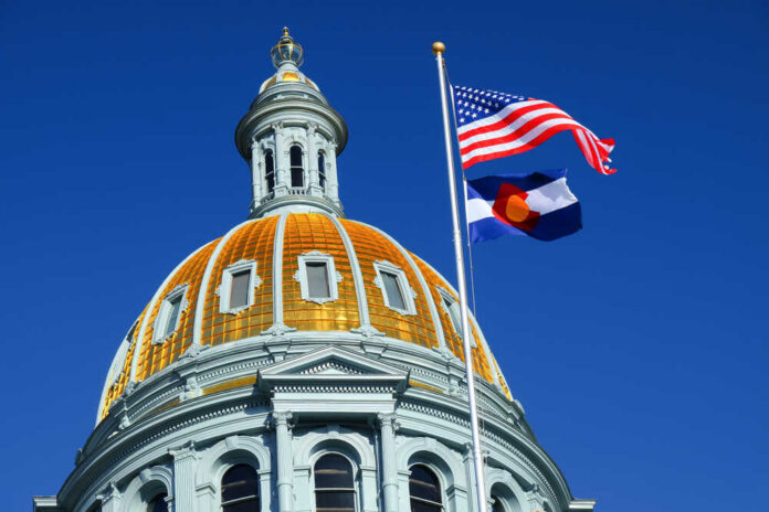 The,American,And,Colorado,Flags,At,The,Colorado,State,Capitol The dome of a state capitol building with flags flying against a blue sky