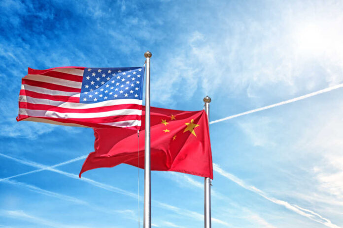 Flags of the United States and China waving against a blue sky