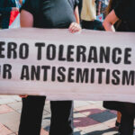 Record Spike in Violent Antisemitic Attacks Protesters holding a sign that reads 'ZERO TOLERANCE FOR ANTISEMITISM'