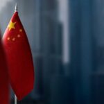 Close-up of the Chinese flag on a flagpole with a blurred urban background