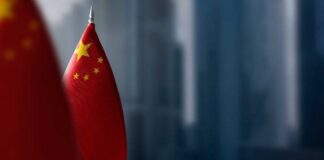 Close-up of the Chinese flag on a flagpole with a blurred urban background