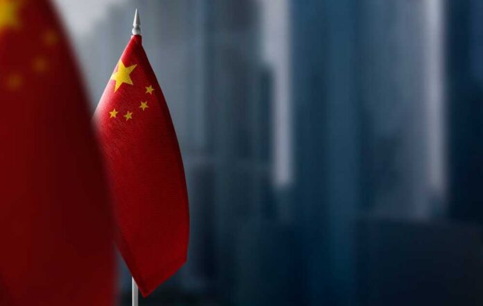 Close-up of the Chinese flag on a flagpole with a blurred urban background