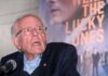An elderly man speaking at a microphone during an event