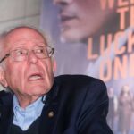 An elderly man speaking at a microphone during an event
