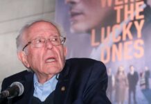 An elderly man speaking at a microphone during an event