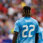 Soccer player wearing a blue jersey with the name Doku and number 22, facing away from the camera