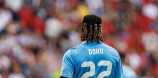 Soccer player wearing a blue jersey with the name Doku and number 22, facing away from the camera
