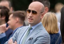 Man in a light suit and sunglasses speaking at an outdoor event