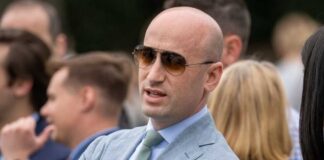 Man in a light suit and sunglasses speaking at an outdoor event