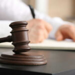 Wooden judge's gavel on a desk with a person writing in the background