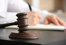 Wooden judge's gavel on a desk with a person writing in the background