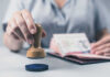 The Court Ruling That Could Reshape H-1B Visas A hand holding a wooden stamp above a passport on a table