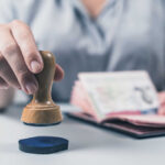 A hand holding a wooden stamp above a passport on a table
