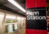 Sign for Penn Station at a subway platform with a moving train in the background