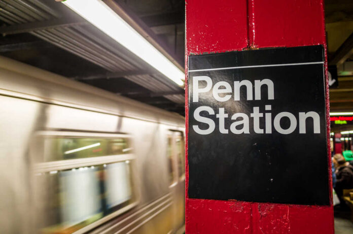 Sign for Penn Station at a subway platform with a moving train in the background