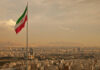 Iran Deal Signed? Not So Fast Iranian flag waving over a city skyline with mountains in the background