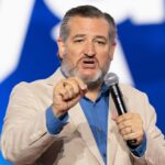 A man in a light suit speaking passionately into a microphone