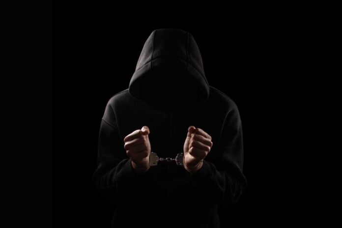 Silhouette,Of,Handcuffed,Male,In,Hoodie,,Dangerous,Criminal,Punished,By A hooded figure with hands in handcuffs against a dark background
