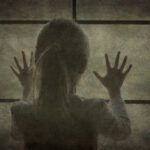 A silhouette of a child with hands pressed against a window