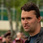 Man speaking outdoors with a crowd in the background