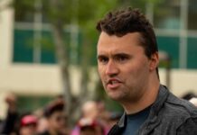 Man speaking outdoors with a crowd in the background