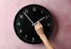America May Finally Stop Changing The Clocks Hand adjusting a wall clock on pink background