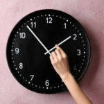 America May Finally Stop Changing The Clocks Hand adjusting a wall clock on pink background