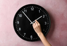 America May Finally Stop Changing The Clocks Hand adjusting a wall clock on pink background