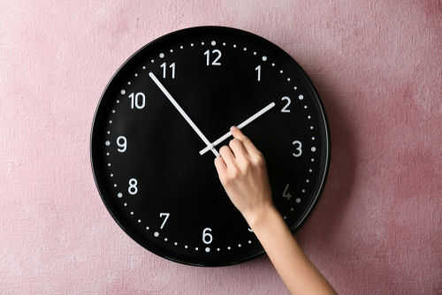 Hand adjusting a wall clock on pink background