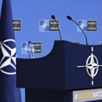 The NATO Promise Faces Reality Check NATO podium with flags and microphones.