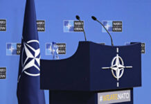 The NATO Promise Faces Reality Check NATO podium with flags and microphones.