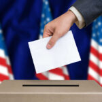 Election Commission Faces Historic Leadership Overhaul Hand placing envelope into ballot box with flag background