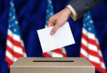 Hand placing envelope into ballot box with flag background