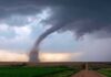 Tornado touching down over open farmland under dark storm clouds