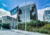 Modern glass office building with blue flag and greenery