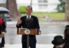Man in suit speaking at outdoor podium with microphones