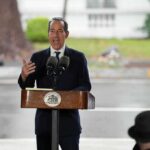 Man in suit speaking at outdoor podium with microphones