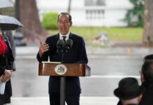 Man in suit speaking at outdoor podium with microphones