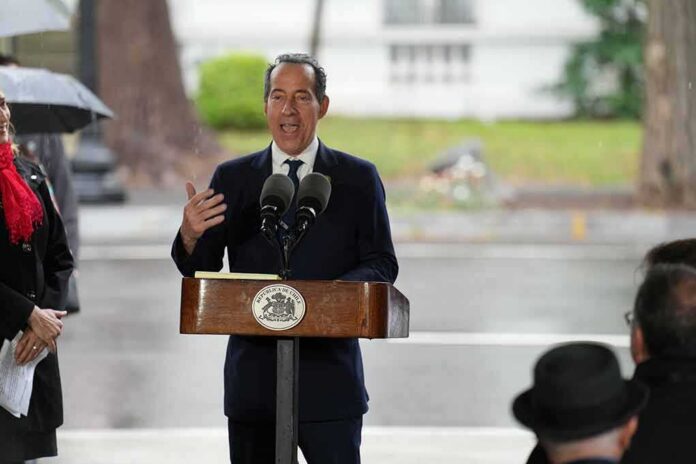 Man in suit speaking at outdoor podium with microphones