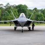 America’s Top Fighter Just Hit A Milestone F-22 Raptor military aircraft on the tarmac with a crew member performing maintenance