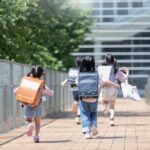 Children with backpacks running on a walkway toward a modern school building
