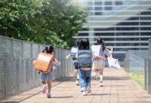 Children with backpacks running on a walkway toward a modern school building