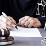 Judge writing at desk with gavel and Lady Justice statue