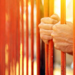 Justice Or Leniency? California Faces Tough Questions Hands gripping orange prison bars with sunlight in the background